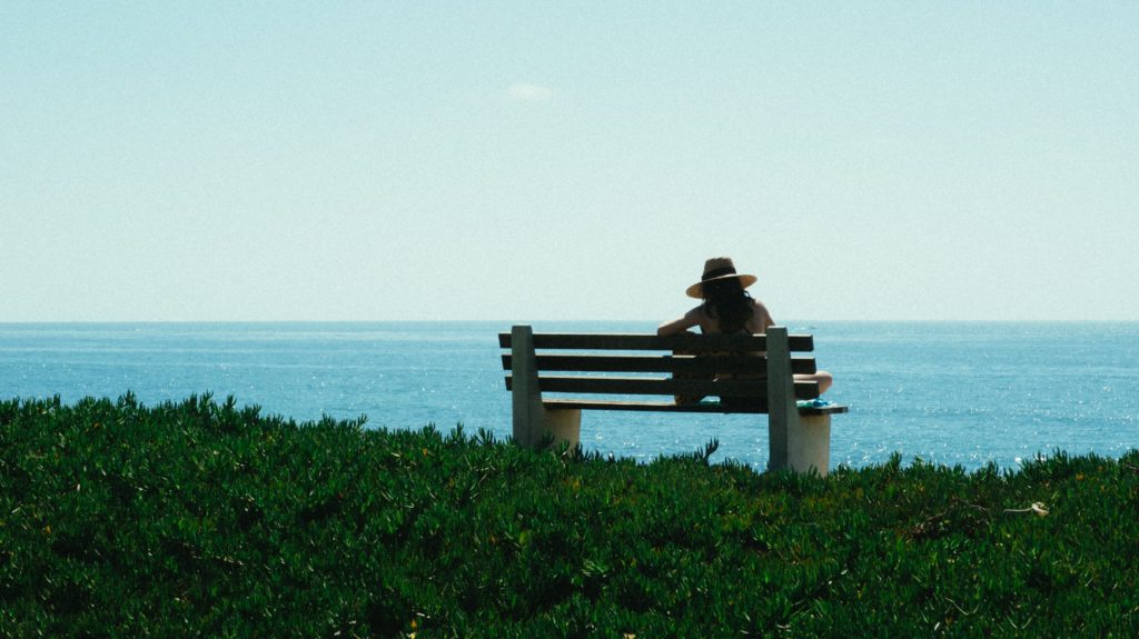mujer sentada sola en un banco mirando al mar