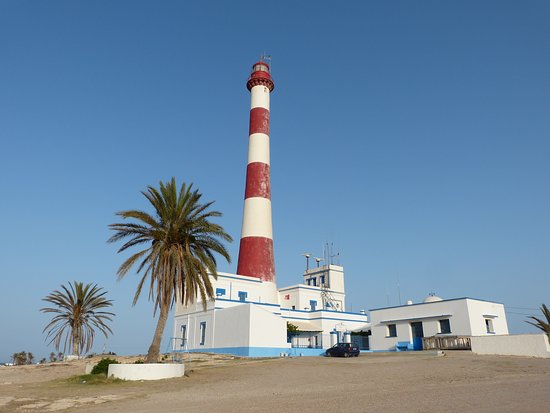 Faro rojo y blanco rodeado de arena y palmeras