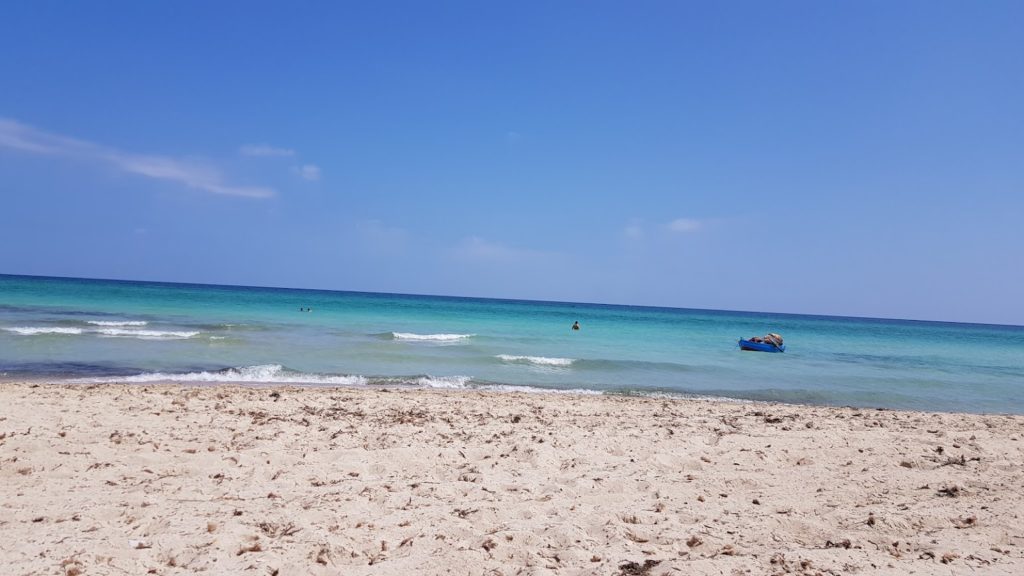 Arena y mar con una pequeña barca en la orilla
