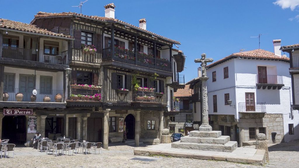 plaza de la alberca con edificio de piedra y madera y cruz de piedra en el centro